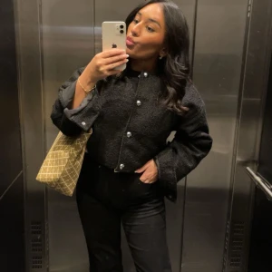 Svart croppad jacka med pärlknappar - Säljer en svart croppad jacka med stora pärlknappar framtill. Jackan har lång ärm och en boxig, lite oversized passform. Perfekt för dig som vill ha en stilren men ändå trendig look.