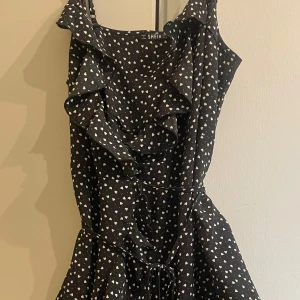 Svart klänning med hjärtmönster  - Supersöt svart klänning med vita hjärtan, volangdetaljer framtill och knyt i midjan, från Shein i storlek M. Aldrig använd🤍 