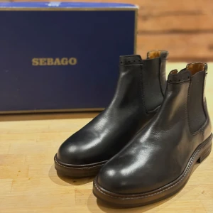 Svarta chelsea boots från Sebago - Stilrena svarta chelsea boots från Sebago i skinn med elastiska paneler på sidorna och rund tå. Perfekta för dig som vill ha en klassisk och tidlös look. Säljes i originalkartong.                                             Skorna är sprillans nya 