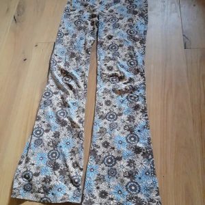 Blommiga utsvängda byxor från Bik Bok - Säljer ett par bruna och blå blommiga byxor från Bik Bok. Byxorna har utsvängda ben och ett retroinspirerat blommönster. Perfekta för dig som gillar färg och mönster! Materialet är mjukt och stretchigt för extra komfort. Använda en gång 