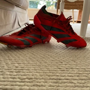 Röda Adidas Predator fotbollsskor (limted edition) - Säljer ett par röda Adidas Predator fotbollsskor med svarta detaljer och snörning. Skorna har en platt sula med dobbar och är perfekta för dig som vill sticka ut på planen. Klassisk design med tydliga Predator-loggor undertill.                         Ny pris 3000+