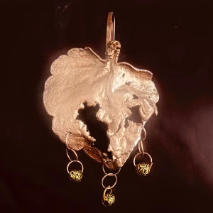 Unikt halsband med bladform och gulddetaljer - Säljer ett halsband med ett stort blad i silverfärg och tre hängande guldfärgade kulor med mönster. Perfekt statement-piece för dig som gillar naturinspirerade smycken och unika detaljer.