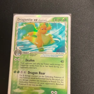 Dragonite ex Delta Species Pokémonkort - Säljer ett Dragonite ex Delta Species Pokémonkort med 150 HP. Kortet har en holografisk yta och visar Dragonite i en dynamisk pose. Kortet har attacker som Deafen och Dragon Roar och är av typ gräs/elfenben.
