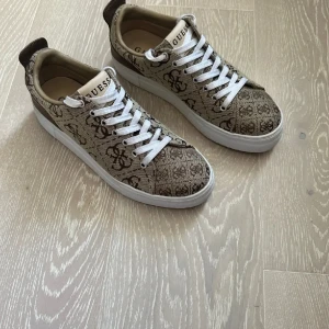 Skor - Giaa Logo Print Low-Top Sneakers från Guess. Köpta i LA förra sommaren och har använts två gånger, som nya. Storleken är 8 1/2 US, alltså 39 i EU💛Perfekta för dig som gillar stilrena och trendiga sneakers.