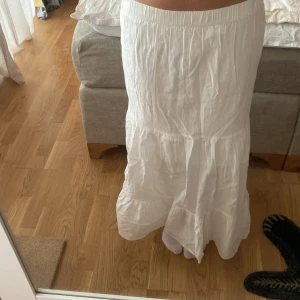 Vit långkjol från Lindex - Säljer en vit långkjol från Lindex med resår i midjan. Kjolen har en luftig och flowy passform med volangdetaljer och är perfekt för varma dagar.
