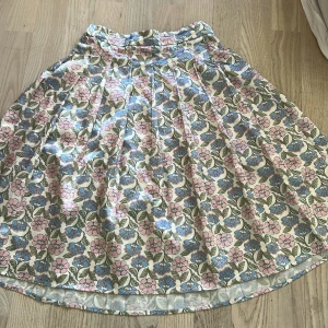 Blommig kjol med pastellfärger - Säljer en vippig kjol med blommigt mönster i pastellrosa, blått och grönt. Kjolen har hög midja och är tillverkad i ett mjukt bomullstyg. Perfekt för dig som gillar färg och mönster!