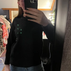 Svart stickad tröja - Säljer en svart stickad tröja med rund halsringning och långa ärmar. Tröjan har en ribbad struktur och är perfekt för kyligare dagar. Enkel och stilren modell som passar till det mesta.