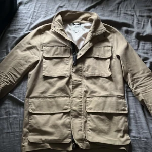 Beige jacka från Kappahl - Stilren beige jacka från Kappahl med fyra stora fickor framtill och dragkedja. Jackan har hög krage och lång ärm, perfekt för vår och höst. Enkel design som passar till många olika outfits. Skick 10/10 använd fåtalgånger. ny pris 1300 mitt pris 950