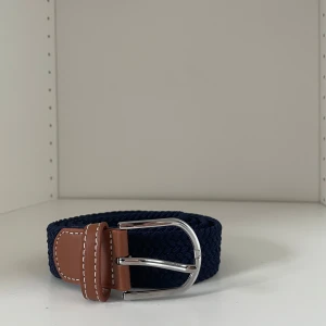 Mörkblått flätat bälte med bruna skinn-detaljer - Snyggt mörkblått flätat bälte med bruna skinn-detaljer och silverspänne. Perfekt accessoar för att lyfta din outfit. Bältet har vita kontrastsömmar på skinnet och klassisk form på spännet. Bältet är 110cm
