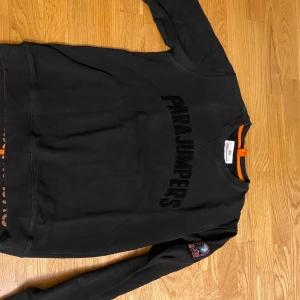 Svart sweatshirt från Parajumpers - Svart sweatshirt från Parajumpers med broderad logga på bröstet och patch på ena ärmen. Tröjan har rund halsringning och ribbade muddar vid ärmslut och nederkant. Perfekt för en avslappnad stil.