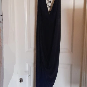 Nwot Marinblå långklänning med ringdetaljer från Club L - Säljer en marinblå långklänning från Club L med djup v-ringning och snygga silverringar framtill. Klänningen är ärmlös och har en figurnära passform, perfekt för festliga tillfällen. Bara, testad. Material viscose och elasthan 