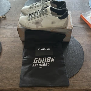 Golden Goose - Golden Goose Superstar sneakers i vitt skinn med grå stjärndetalj på sidan, grå snörning och svart hälparti. Klassisk låg modell med rund tå och platt sula. Snygga och stilrena skor med ikonisk design. Vid frågor och funderingar så tveka inte att skriva ;)
