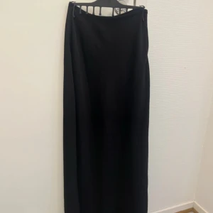 Svart långkjol - Säljer en svart långkjol med diskret dragkedja på sidan. Kjolen har en rak och enkel design som ger en stilren look. Från new yorker stl 36