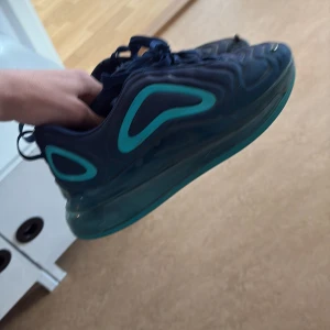 Nike Air Max 720 sneakers i blått och turkost - Säljer ett par Nike Air Max sneakers i mörkblått med turkosa detaljer och genomskinlig sula. Skorna har snörning och en sportig design med rund tå och platt sula. Perfekta för dig som gillar streetwear och vill sticka ut med färg.