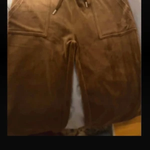 Bruna juicy byxor i velour - Säljer ett par bruna mjukisbyxor i mjuk velour med raka ben och dragsko i midjan. Byxorna har stora fickor framtill och en avslappnad passform. Perfekta för en chill och bekväm stil.