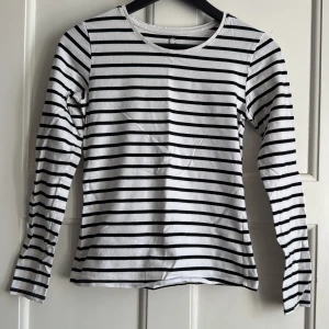 Randig långärmad tröja från C - Säljer en klassisk vit långärmad tröja med svarta horisontella ränder från märket C. Tröjan har rund halsringning och är i ett mjukt bomullsmaterial. Perfekt för en stilren och enkel look.