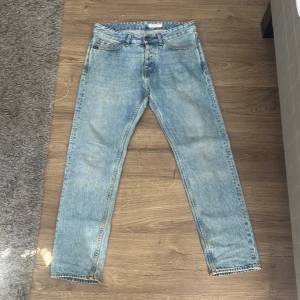 Ljusblå jeansbyxor från Tiger of Sweden - Säljer ett par klassiska ljusblå jeans från Tiger of Sweden, modell NICO. Jeansen har raka ben, fem fickor och snygga kontrastsömmar. Perfekta för dig som gillar stilrena och tidlösa jeans med modern passform.