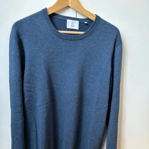 Blå stickad tröja från Bläck - Säljer en stilren blå stickad tröja från Bläck i storlek L. Passar 180 cm och uppåt. 