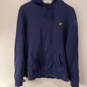 Lyle & Scott Marinblå hoodie - Säljer en mörkblå hoodie från Lyle & Scott med klassisk gul broderad logga på bröstet. Tröjan är i bra skick och kommer inte till användning, eftersom den inte passar längre. Skriv i dm för frågor! 