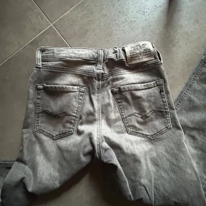 Grå jeansbyxor från Replay - Säljer ett par grå jeansbyxor från Replay, modell THAD. Klassisk femficksdesign med raka ben och normal passform. Snyggt Replay-märke bak i midjan och diskreta sömmar på bakfickorna. Perfekta till vardags för en stilren look.