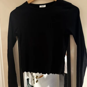 Svart långärmad croppad tröja från Kappahl - Säljer en svart långärmad croppad tröja från Kappahl. Tröjan har rund halsringning och en enkel, stilren design med vågig kant nertill. Perfekt till många olika outfits!