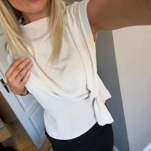 Vit omlottopp med knyt - Snygg vit omlottopp med knyt i sidan och draperad halsringning. Toppen har en elegant och stilren design som passar perfekt till både jeans och kjol. Materialet känns mjukt och följsamt.