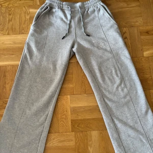 Grå baggy mjukisbyxor - Säljer ett par grå mjukisbyxor med bred passform. Byxorna har broderad logga på ena benet och snörning även vid benslut. Perfekta för en avslappnad stil. Pris går att diskutera och ställ frågor!