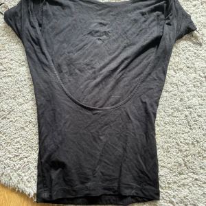 Svart topp med djup rygg från Gina Tricot - Svart, tight topp från Gina Tricot i mjuk bomull med korta ärmar och en djup, rundad rygg. Perfekt för att skapa en stilren och enkel look. Storlek XS.