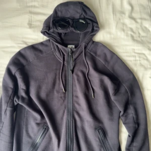 Mörkblå hoodie med  från C.P. Company - Säljer en mörkblå hoodie från Cp company. Hoddien har två fickor med dragkedja och är tillverkad i mjuk fleece. Användt skick men inga hål eller märken. 