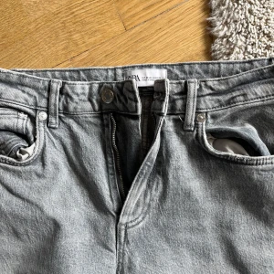 Grå jeans från Zara - Säljer ett par grå jeans från Zara med klassisk femficksdesign och dragkedja. Byxorna har raka ben med slits och en lätt tvättad look. Perfekta för en avslappnad stil. Lite slitna längst ner, se bild.
