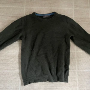 Mörkgrön kashmirtröja från John Lewis MEN - Säljer en mörkgrön rundhalsad tröja i 100% kashmir från John Lewis MEN. Tröjan har långa ärmar och ribbade muddar vid hals, ärmslut och nederkant. Perfekt för dig som gillar klassisk och stilren design. På sista bilden ser man att det är hål därav priset 