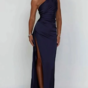 Mörkblå långklänning med slits och oneshoulder - Säljer en elegant mörkblå långklänning i satin med hög slits och oneshoulder-design. Klänningen har draperad midja och smal passform som framhäver figuren. Perfekt för bal eller fest.