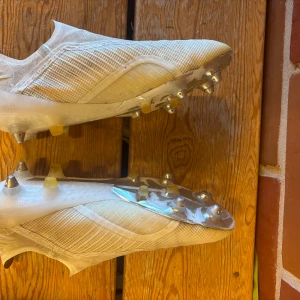 Vita fotbollsskor från Adidas utan snörning - Säljer ett par vita fotbollsskor från Adidas, skruvdubbar och har använts några gånger men för det mesta bara varit liggades. Storlek 43,5. 
