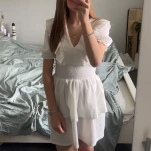 Vit kortklänning med volang och v-ringning - Säljer en söt vit klänning med puff ärmar. Mycket bra skick och har bara använts en gång. Storlek xs💕