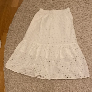 Vit kjol med broderade detaljer - Säljer en vit kjol med broderade hål och volang nertill. Kjolen har resår i midjan. Jättesöt nu till sommaren. Användt en gång💕
