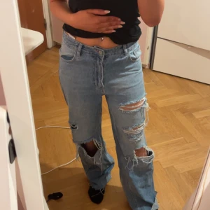 Ljusblå ripped jeans från ZDN - Säljer ett par ljusblå jeans från ZDN med flera stora slitningar och hål på benen. Byxorna har normal passform och raka ben, klassisk femficksmodell och knappgylf. Perfekta för en avslappnad och trendig look.