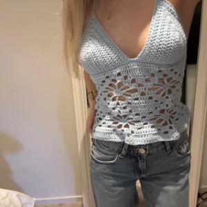 Ljusblå egenvirkad halterneck-topp - Superfin ljusblå egenvirkad topp med halterneck och knyt i ryggen. Toppen har ett blommigt mönster, perfekt för sommaren! Banden är justerbara så passar därför flera storlekar.