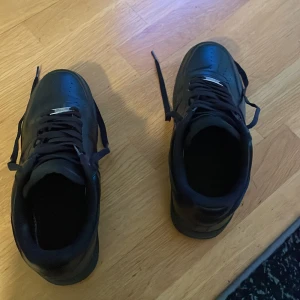 Svarta Nike Air Force 1 sneakers - Säljer ett par helsvarta Nike Air Force 1 sneakers. Klassisk modell med rund tå, snörning och platt sula. Skorna är i syntetmaterial och passar perfekt till dig som gillar stilrena och tidlösa sneakers.