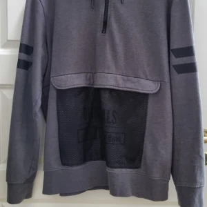 Grå hoodie från Sons of Owen - Säljer en grå hoodie från Sons of Owen i storlek XL. Tröjan har svarta detaljer på ärmarna, dragkedja vid halsen och en stor meshficka framtill. Perfekt för en avslappnad stil.