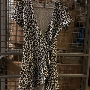 Leopardmönstrad omlottklänning från Divided - Säljer en snygg leopardmönstrad omlottklänning från Divided. Klänningen har korta ärmar, v-ringning och knyt i midjan. Perfekt för dig som vill sticka ut med ett djurmönster och gillar trendiga detaljer.