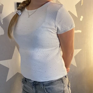 Vit ribbad topp med små glittriga stenar från H&M Divided - Säljer en vit ribbad topp från H&M Divided med korta ärmar och små glittriga stenar över hela tyget. Toppen har en rund halsringning och är i stretchigt material som sitter snyggt på kroppen.