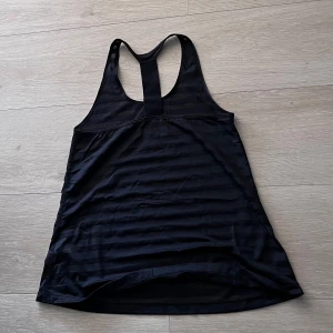 Svart träningslinne med brottarrygg - Säljer ett svart träningslinne med brottarrygg. Perfekt för gymmet eller löprundan, tillverkat i ett lätt och ventilerande material som håller dig sval under passet.