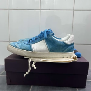 Valentino Flycrews - Säljer ett par snygga Valentino sneakers i blå mocka med vita paneler och blå skosnören. Skorna har rund tå och platt sula, perfekt för en trendig vardagslook. Kommer med originalpåse och extra skosnören.