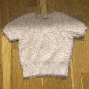 Zara ”t-shirt” - Supermjuk och fluffig ljusrosa tröja från ZARA. Tröjan har korta ärmar och rund halsringning, perfekt för en mysig och trendig look. 