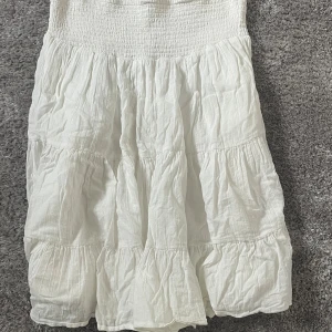 Vit Volangklänning  - Säljer en vit klänning med smock upptill och volanger. Klänningen är tillverkad i ett lätt och luftigt material, perfekt för varma dagar. Den har en avslappnad passform och kort. 