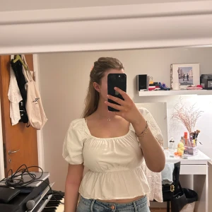 Vit puffärmad blus från BikBok - Säljer en söt vit blus från BikBok med puffiga korta ärmar och resår i midjan. Toppen har fyrkantig ringning och volang nertill. Perfekt att matcha med jeans eller kjol! Säljer då den ej kommer till användning.