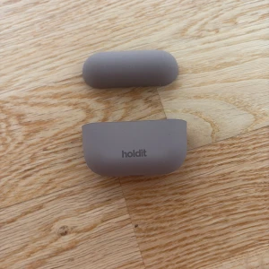 Fodral till trådlösa hörlurar från Holdit - Säljer ett beige fodral till trådlösa hörlurar från Holdit. Fodralet är gjort i mjukt syntetmaterial och har en enkel design.Perfekt för att skydda dina hörlurar och hålla dem fräscha. Har inga defekter och är andvänt ett fåtal gånger.