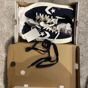 Mörkblå sneakers från Converse - Säljer ett par mörkblå Converse sneakers med vita detaljer och stjärnlogga på sidan. Skorna har vita snören, platt sula och rund tå. Perfekta för en avslappnad stil och passar till jeans eller shorts. Pris kan diskuteras vid smidig affär:). 