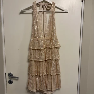 Champagnefärgad paljettklänning med volanger från SHEIN - Supersnygg kort klänning från SHEIN i champagnefärg med massor av paljetter och volanger. Djup v-ringning och öppen rygg med knyt i nacken. Perfekt för dig som vill sticka ut med glitter och glamour!