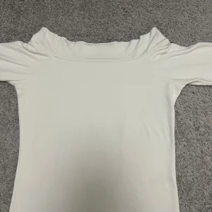 Vit långärmad topp med volangkrage från BikBok - Säljer en vit långärmad topp från BikBok med en snygg volangkrage. Toppen är i ett mjukt material och har en figurnära passform. Perfekt att styla med jeans eller kjol för en trendig look. Toppen är off-shoulder men skulle definitivt kunna användas som en vanligt tröja. Finast som off-shoulder!
